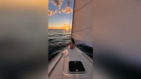 Young woman in pink outfit relaxing on a sailboat at sunset during a peaceful ocean voyage.