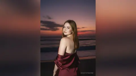 ShantayMayne poses against a sunset beach backdrop wearing a red satin slip dress.
