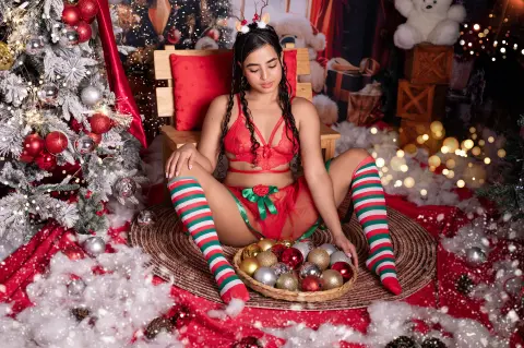 Young woman in red lace lingerie and striped stockings sitting in a festive Christmas setting.
