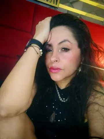 Woman in a black sleeveless top with jewelry posing against a red background for a moody portrait.