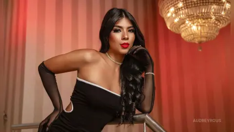 Elegant woman in a black strapless dress and long gloves posing glamorously in a warm, red-lit room.