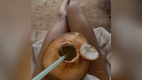 LucyMartin rests on a white towel while holding a cracked open coconut with a straw.