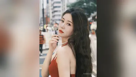Young woman in a red dress with long wavy hair posing on a city street during golden hour.