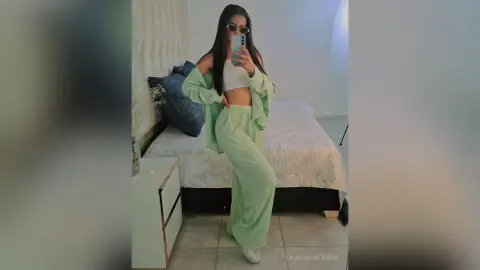 Young woman in mint green lounge set taking a mirror selfie in a bright bedroom.