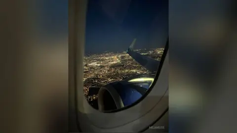 Night view of city lights through an airplane window overlooking a glowing urban landscape from a flight.