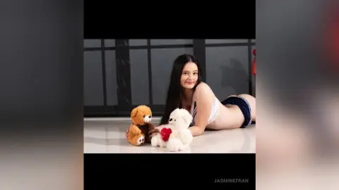 Young woman in white lingerie relaxing on a floor with a brown and a white teddy bear in a bright studio.