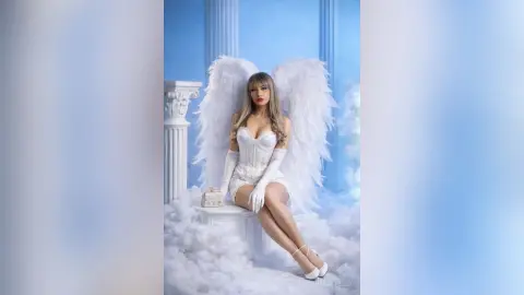 NatashaCastello poses as an angel with large white wings, wearing a white corset and gloves while sitting on clouds.