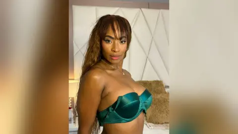 Beautiful woman in a green satin bra posing confidently in a bright bedroom setting.