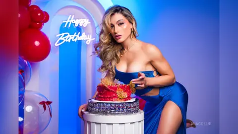 Glamorous woman in a blue dress celebrating a birthday with a red cake and balloons in a blue studio setting.