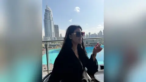 Stylish woman in black outfit and sunglasses relaxing on a luxury balcony overlooking the Dubai skyline.
