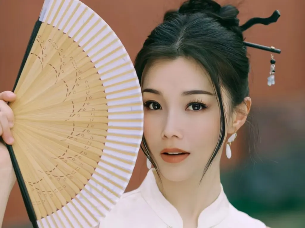 Elegant woman in traditional white Hanfu holding a vintage folding fan in a serene outdoor setting.