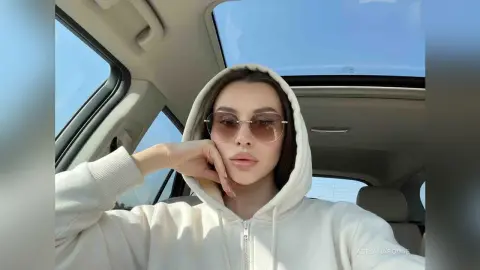 Young woman in a white hoodie and sunglasses relaxing in a car with a sunroof on a sunny day.