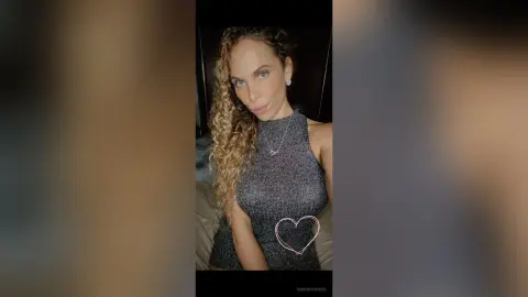 Glamorous woman with curly hair wearing a sparkly silver halter top in a moody indoor setting.