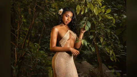 Beautiful woman in a gold crochet halter dress posing in a lush tropical jungle setting.