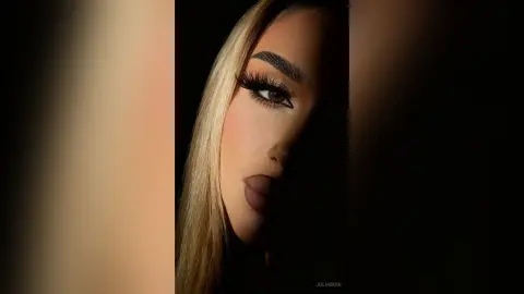 Close-up portrait of a blonde woman with dramatic winged eyeliner and glamorous makeup in moody lighting.