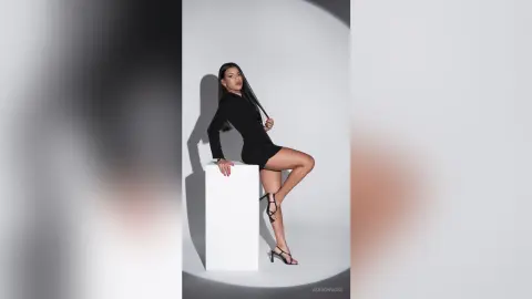 Elegant woman in a chic black long-sleeve mini dress posing confidently against a minimalist white studio background.