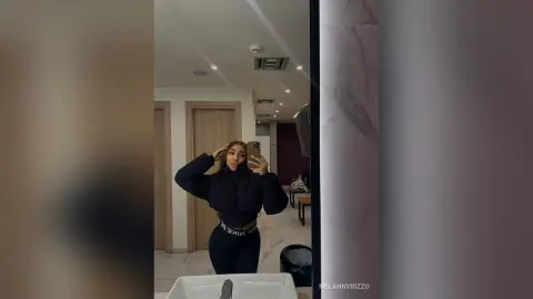 Stylish woman in a black cropped jacket and Nike leggings taking a mirror selfie in a modern bright apartment.