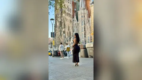 Stylish woman in a black dress standing on a city street near the Sagrada Familia in Barcelona.