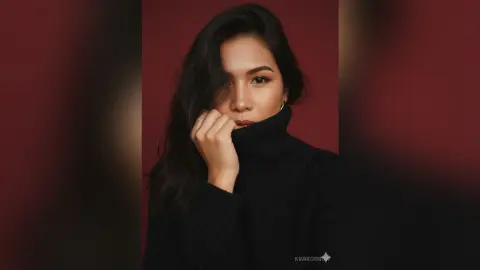 Elegant woman in a black turtleneck sweater posing against a moody dark red background.