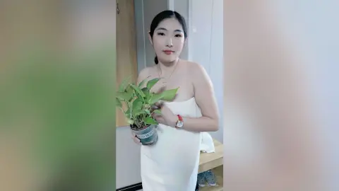 Young woman in a white strapless dress holding a green potted plant in a bright indoor setting.