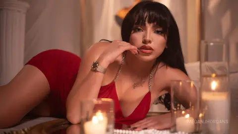 Glamorous woman in a red dress lounging by glowing candles in a romantic, moody setting.