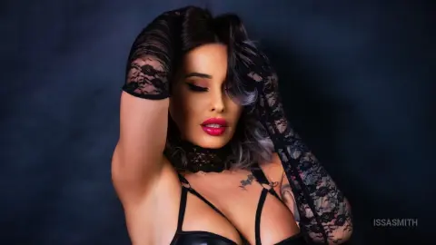 Glamorous woman in a black lace outfit posing against a dark moody background.