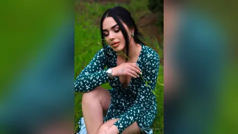 Young woman in a green floral dress holding a wildflower in a lush green meadow with a dreamy mood.