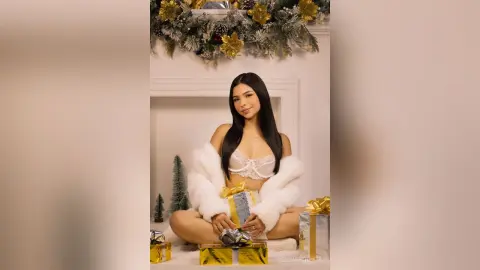 Smiling woman in a white faux fur coat sitting by Christmas gifts in a festive holiday setting.