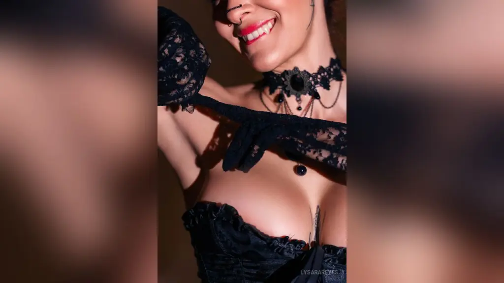 LysaraReyes lies naked on red sheets surrounded by lit candles, showing her tattoos and red hair.