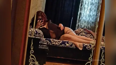 Woman in black loungewear relaxing on a patterned daybed in a moody, dimly lit room.