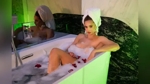 Young woman relaxing in a bubble bath in a luxury marble bathroom with moody green lighting.