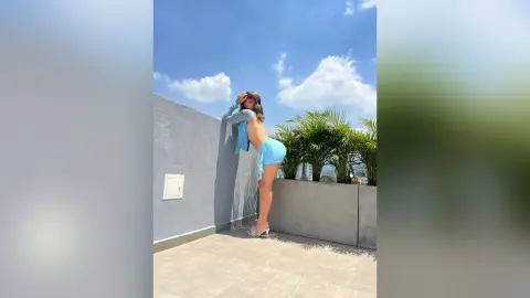 Young woman in a light blue summer outfit posing on a sunny rooftop balcony.