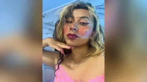 Woman with glamorous makeup and pink lace outfit posing with a dreamy, glowing aesthetic.