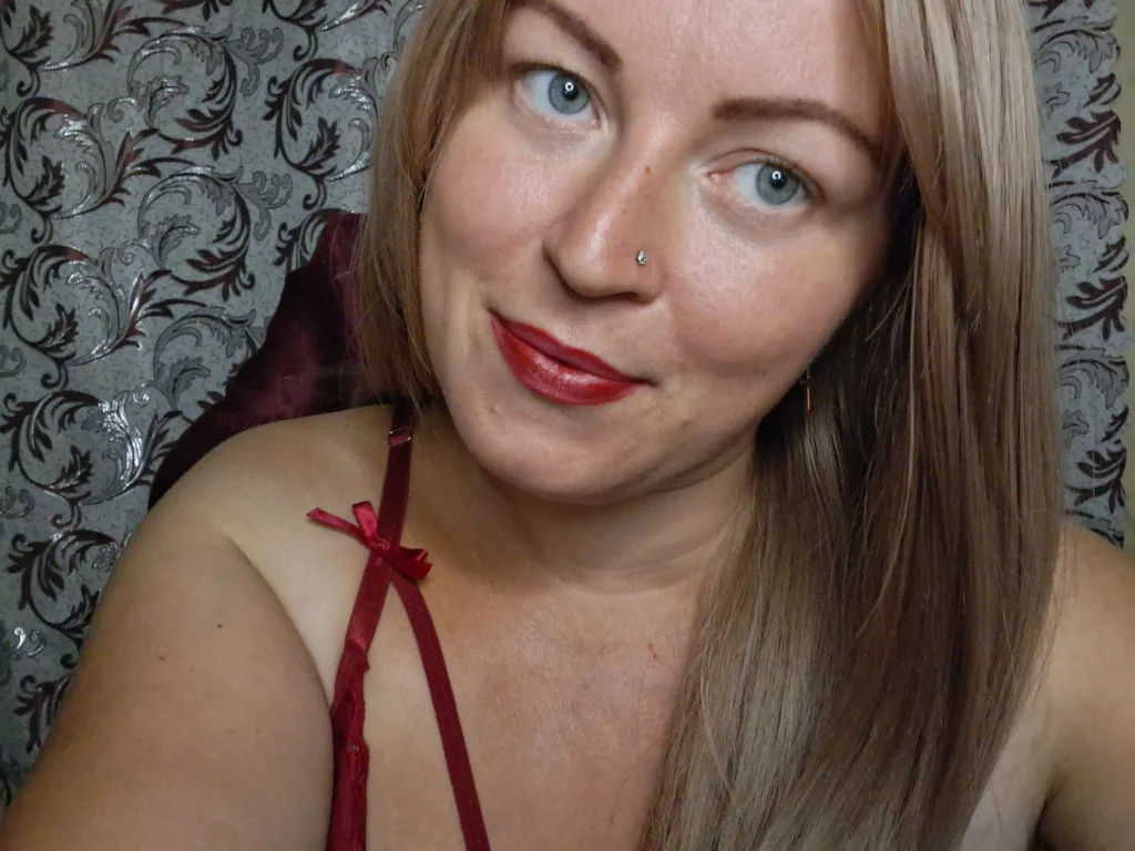 Creativepersonality poses in a light purple tank top, showing her dark hair and bare shoulders against a red background.