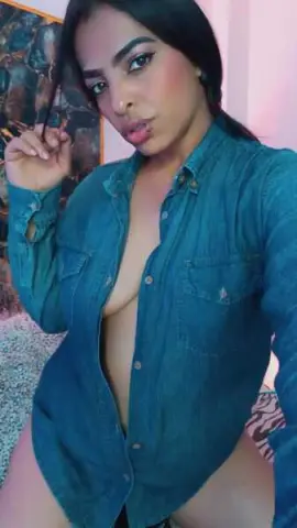 Young woman in a blue denim shirt posing with a confident expression in a cozy indoor setting.