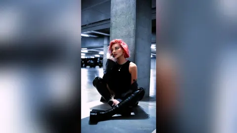 MarianBells — MarianBells sits on a concrete floor in a dark parking garage wearing a black tank top and tall black boots.