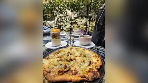 Delicious gourmet pizza and a creamy latte served on a cafe table in a lush outdoor garden setting.