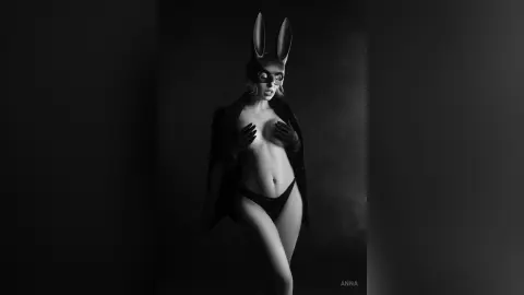 Moody black and white portrait of a woman in bunny ears and dark lingerie against a dark background.