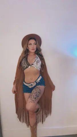 Ameliajade111 — Woman in boho western outfit with cowboy hat, paisley bikini top, denim shorts, and fringed brown cardigan.