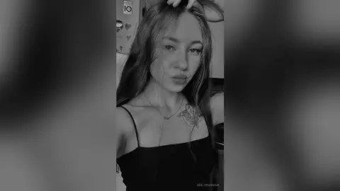 Young woman with long hair wearing a black tank top posing for a moody black and white portrait.