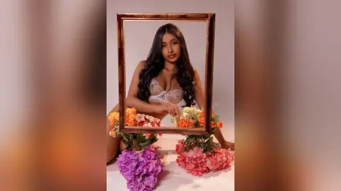 Beautiful woman in white lace lingerie posing behind a gold frame surrounded by colorful spring flowers.