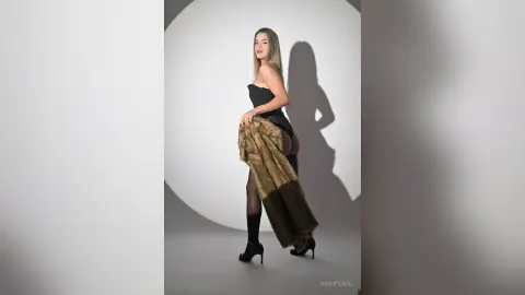 Elegant woman in a black strapless bodysuit and faux fur coat posing in a minimalist studio setting.