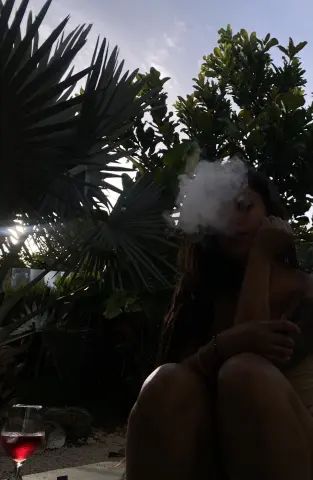 Young woman relaxing outdoors amidst tropical palm trees with a dreamy, hazy atmosphere.