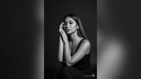 Elegant woman in a black sleeveless top posing with a moody, sophisticated expression in a black studio setting.