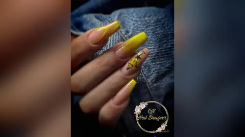 Close-up of long coffin-shaped nails with yellow ombre design and black star nail art over denim fabric.