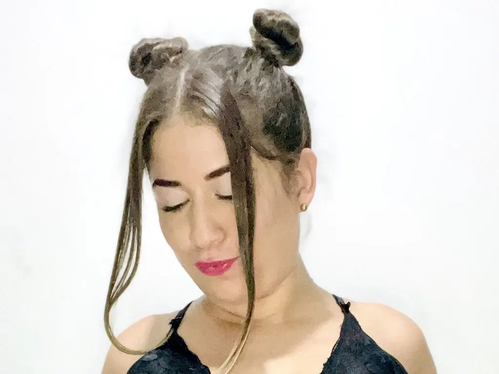 Young woman with space buns hairstyle and dark lace top posing against a white background.