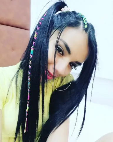Smiling young woman with long black hair and colorful hair extensions wearing a yellow t-shirt.
