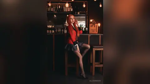 AllisonKron sits on a bar stool wearing a red blazer and a plaid skirt with black tights.