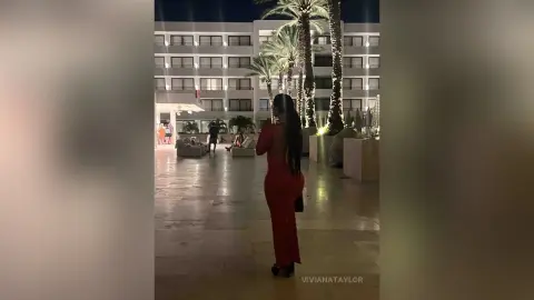 Woman in an elegant red evening gown standing on a luxury resort terrace at night.