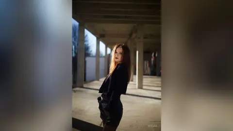 Stylish woman in a black blazer and shorts posing in a moody, sunlit concrete urban corridor.